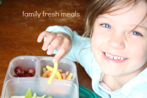 child sitting with a lunchbox, eating snacks