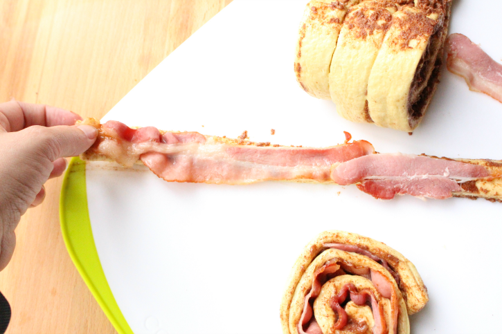 laying a strip of bacon on an unrolled cinnamon roll