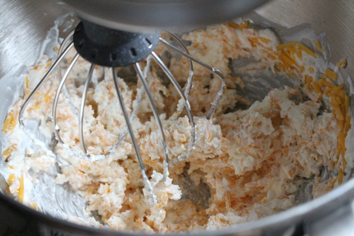 cream cheese, sour cream, salt and cheddar cheese being mixed in a stand mixer