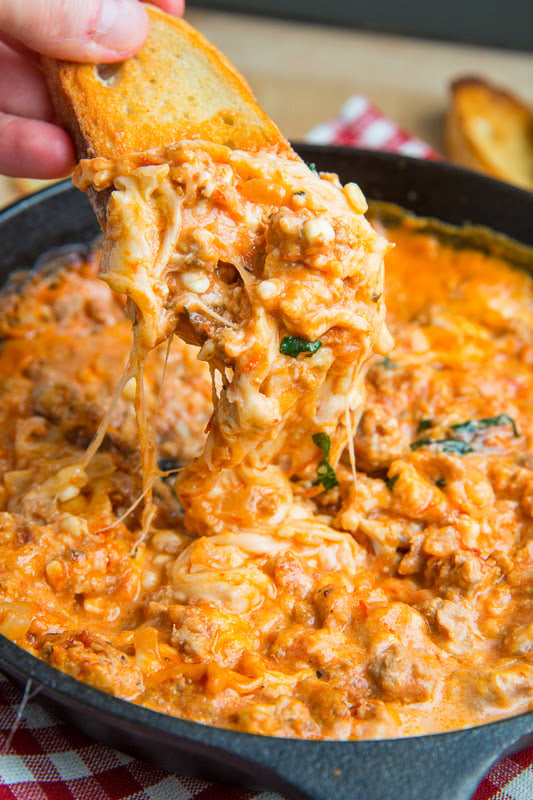 Lasagna Dip in a cast iron skillet with a piece of bread scooping up some