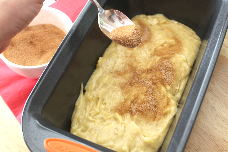 Cinnamon Swirl Banana Bread batter in a bread pan, being sprinkled with cinnamon sugar