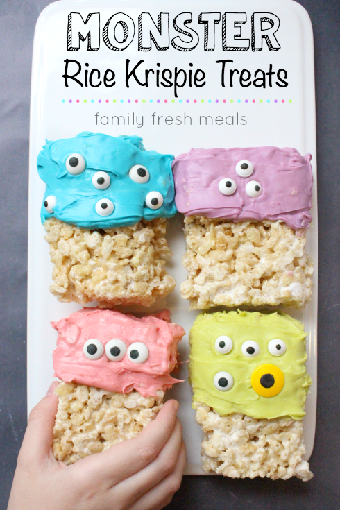 Easy Halloween Monster Rice Krispie Treats on a plate with a hand taking one