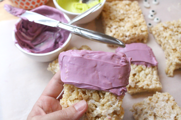 spreading colored frosting on the top half of rice Krispy treats
