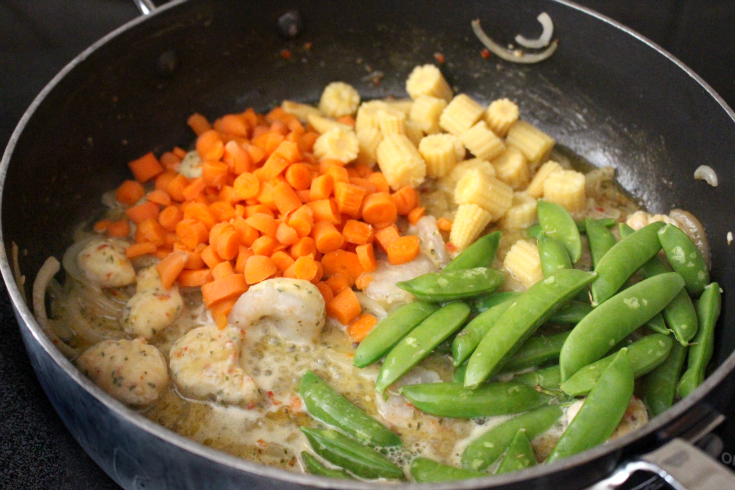 Chopped carrots, baby corn, sugar peas and shrimp being added to the pan