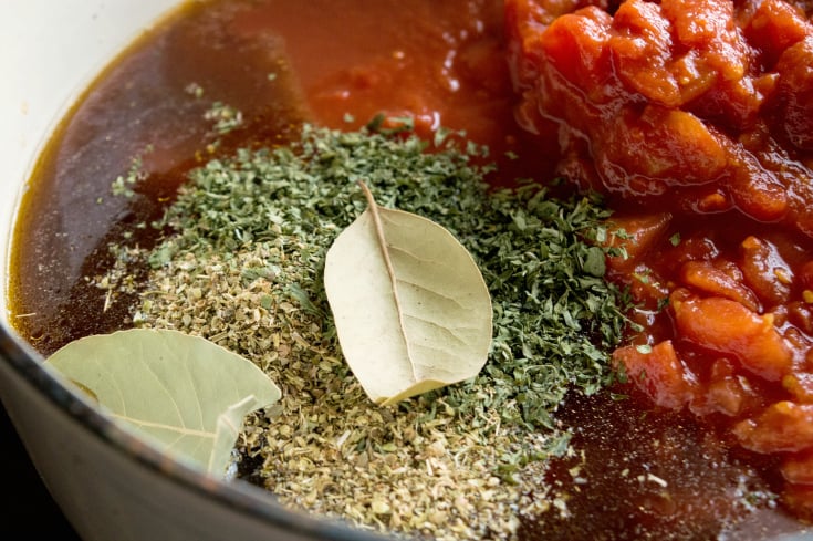 Grandma's Easy Goulash Recipe - Seasonings, broth, tomatoes and bay leave in a dutch oven