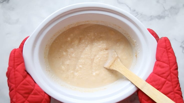 Crockpot Cheesy Grits and Shrimp - Oven mitts holding a white slow cooker filled with grits