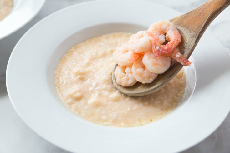 Crockpot Cheesy Grits and Shrimp - Wooden spoon placing shrimp on grits