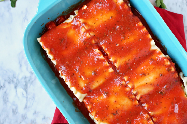 Cheesy Lasagna Rolls - Lasagna rolls in a blue pan with sauce on top