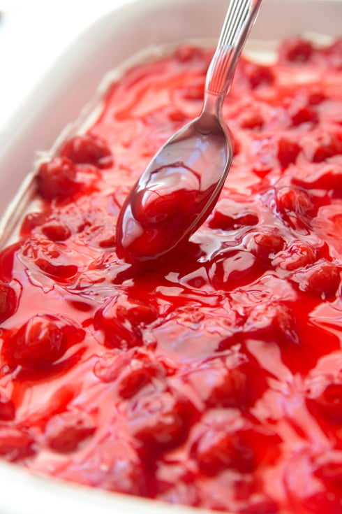 No Bake Cherry Cheesecake Dessert - Spooning cherry topping on top of dessert