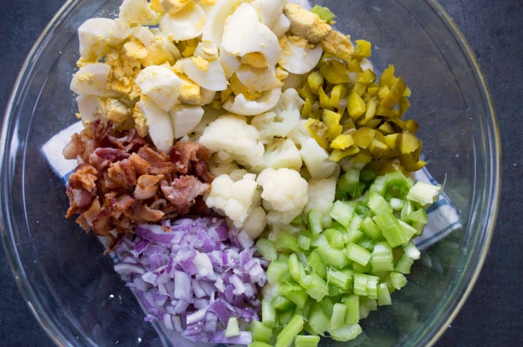 Cauliflower Potato Salad - hard boiled eggs, cauliflower, bacon, pickles, celery and onion in a glass bowl