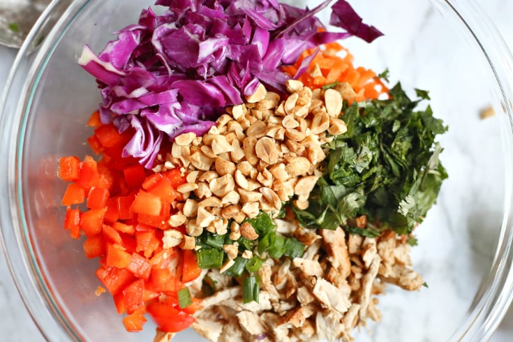 Creamy Thai Chicken Salad - Bell pepper, peanuts, onions, red cabbage, diced chicken, cilantro, peanuts, carrots and bell pepper together in a glass bowl