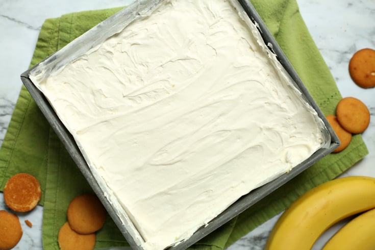Easy Banana Cream Pie Bars - cream topping on of banana pudding layer in a square baking dish