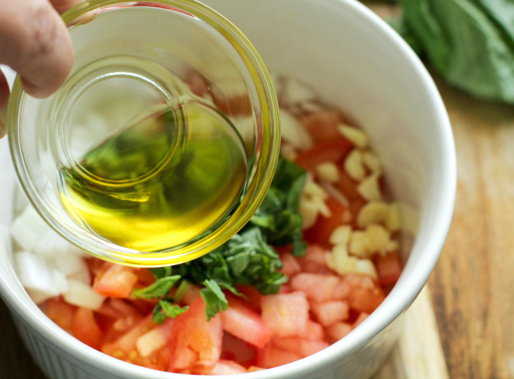 Easy Fresh Bruschetta Recipe - Oil being poured over chopped tomatoes, onion, garlic and basil