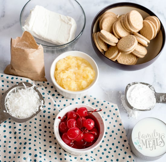 Pina Colada Lush Cake - Ingredients on a marble counter- cherries, vanilla oreos, milk, powdered sugar, cream cheese, pineapple, coconut, jello mix