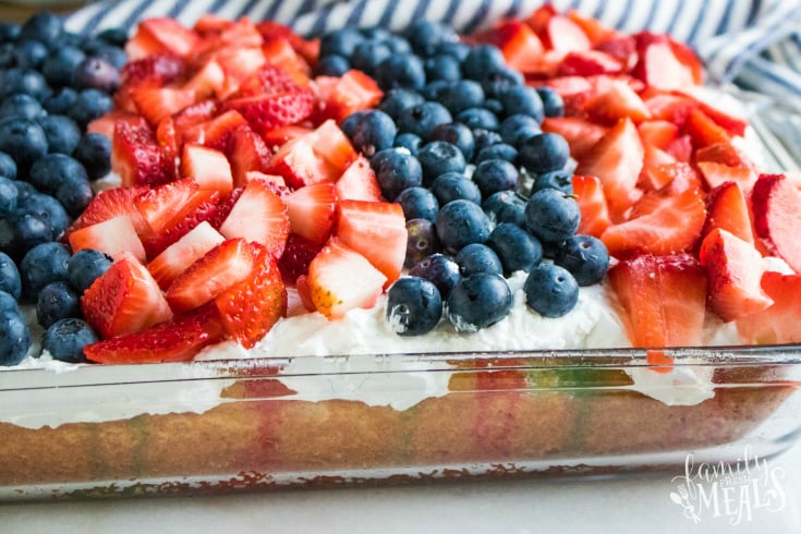 Red White and Blue Poke Cake - Fresh strawberry and blueberries placed on top of a white cake, in a glass baking dish