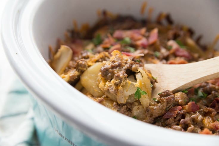 Crockpot Cheesy Cowboy Potatoes - cooked casserole being scooped with a wooden spoon