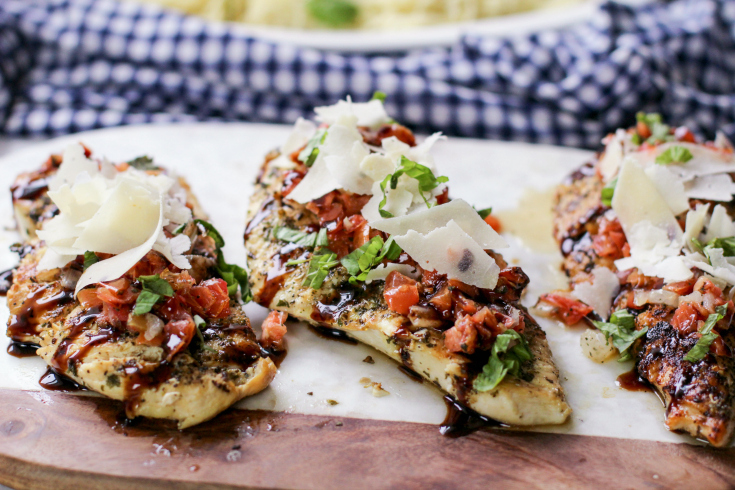 Bruschetta Chicken - Chicken breast on cutting board, topped with bruschetta, parmesan cheese and parsley - Family Fresh Meals