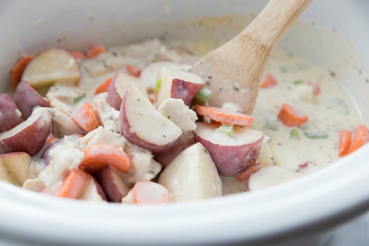 Creamy Crockpot Chicken Vegetable Soup - Stirring soup ingredients with wooden spoon
