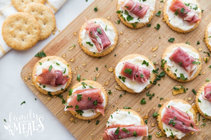 Easy Creamy Prosciutto Cracker Appetizer - Appetizers on a cutting board, drizzled with honey and parsly