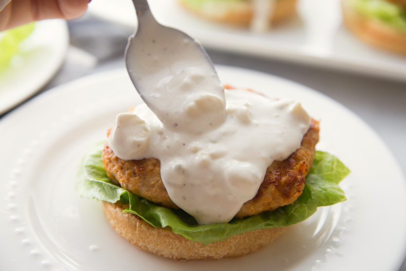 Buffalo Chicken Burgers - spooning blue cheese dressing on top of burger