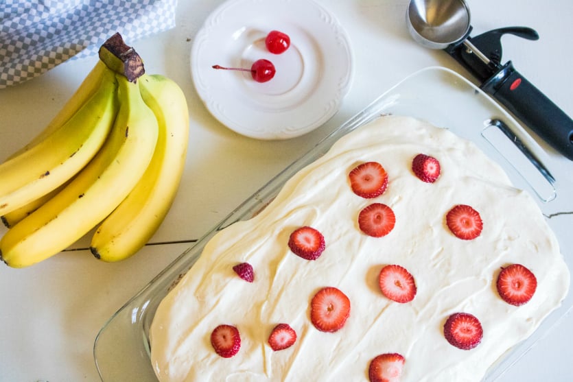 Banana Split Poke Cake - frosted cake topped with sliced strawberries