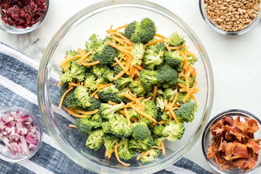 Creamy Broccoli Salad - Ingredients in bowls broccoli, shredded cheese, seeds, bacon, onions and cranberries