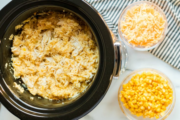 Crockpot Creamy Chicken and Rice - Cooked chicken and rice in slow cooker with a side of corn and cheese in bowls