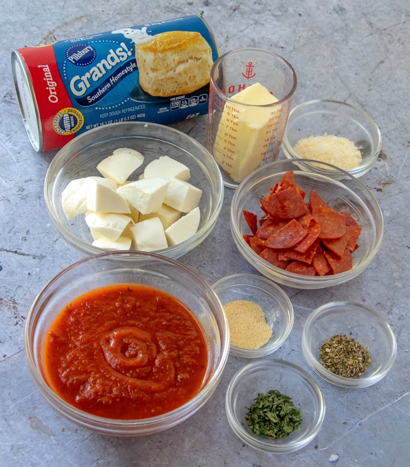 Cheesy Pizza Bombs - ingredients on counter - biscuits, cheese, butter, pepperoni, seasoning, marinara sauce. 