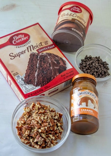 Chocolate Turtle Poke Cake - Ingredients on table - chopped nuts, cake mix, caramel sauce and frosting