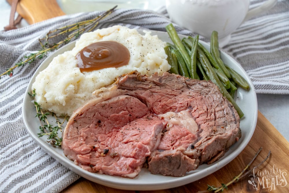 The Best Prime Rib - sliced prime rib on a plate with mashed potatoes and green beans