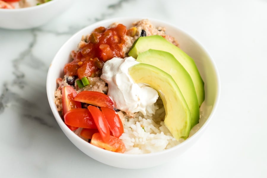 Crockpot Cilantro Lime Chicken - chicken burrito bowl severed with sour cream, sliced avocado, salad and tomatoes