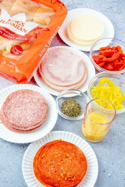 How to Make Hot Italian Sub Sliders - ingredients on the table. Deli slices, seasoning, peppers, melted butter and rolls