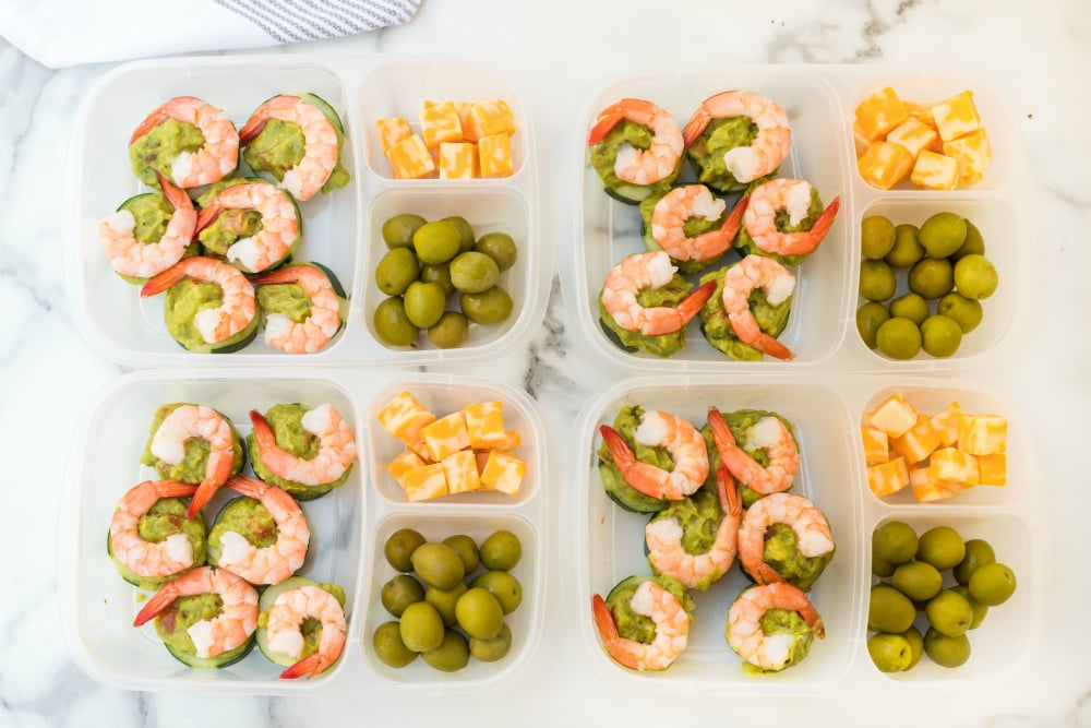 Top down photo of 4 easy lunchboxes with Shrimp Avocado, guacamole, olives and cheese cubes