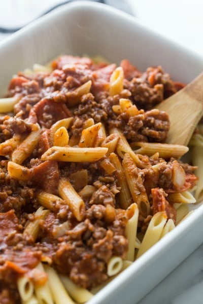 Easy Pizza Pasta Bake - pouring meat and sauce mixture over cooked noodles