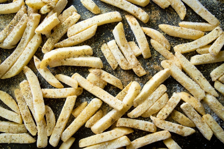 Frozen fries on baking sheet with seasoning