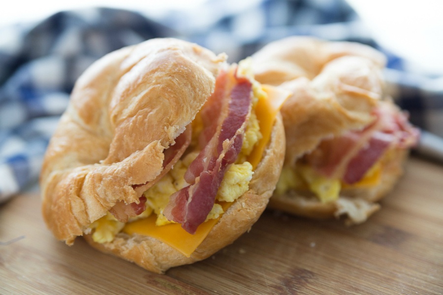 Freezer Friendly Breakfast Croissant Sandwiches - two bacon egg and cheese breakfast sandwiches on a cutting board