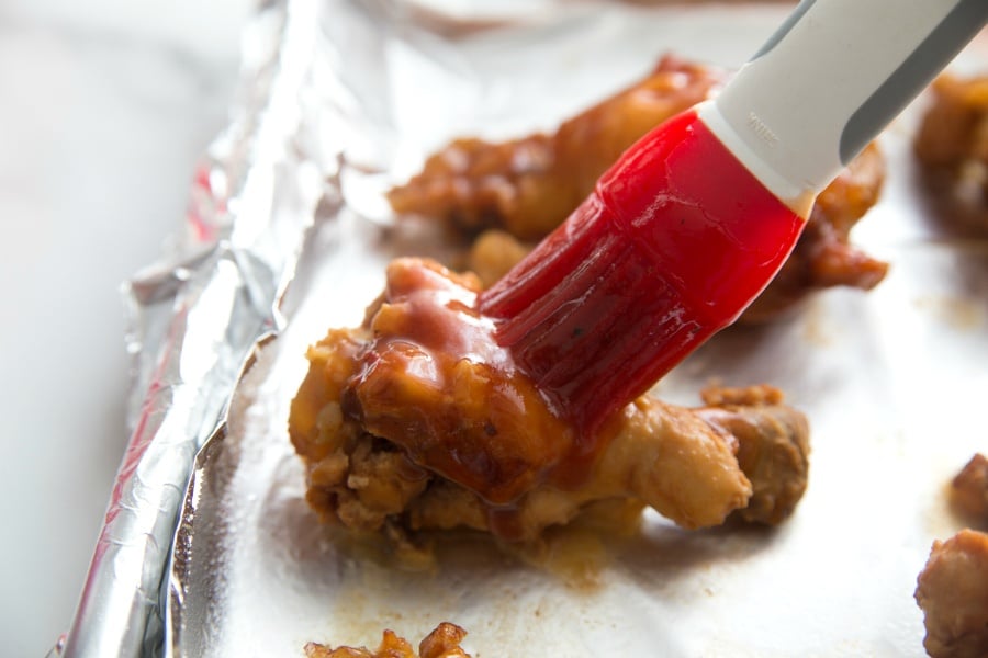 Chicken wings on a baking sheet being brushed with sauce