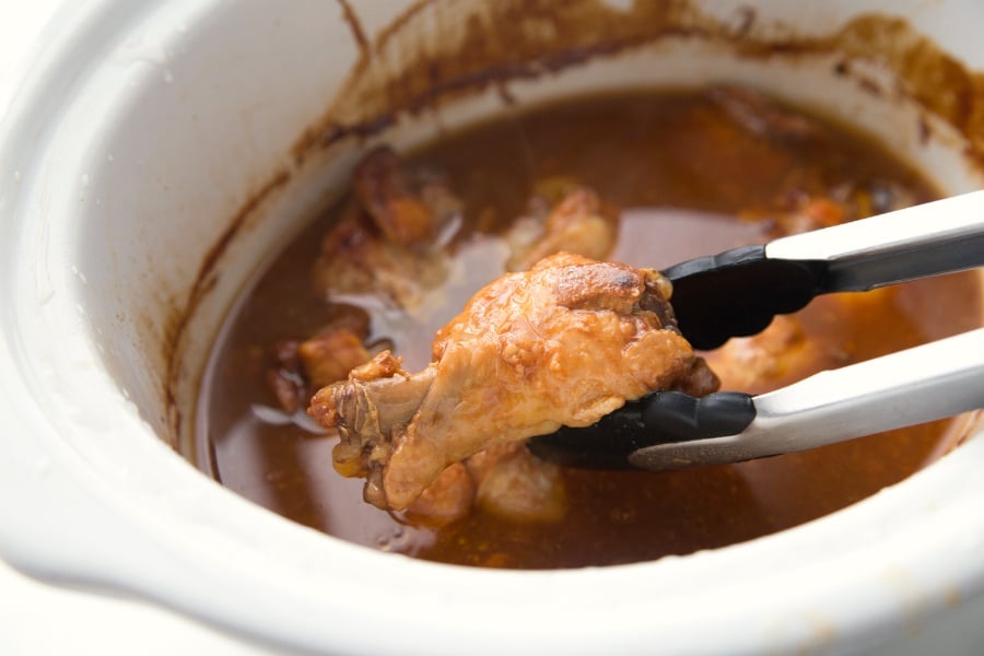 Food tongs picking up a chicken wing from the crockpot