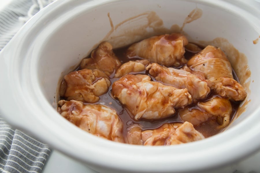 Raw chicken wings in a white crockpot and sauce