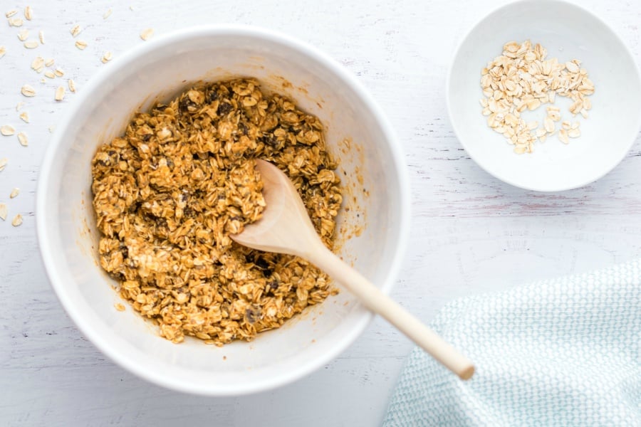 Energy bites ingredients mixed together in a white bowl with wooden spoon