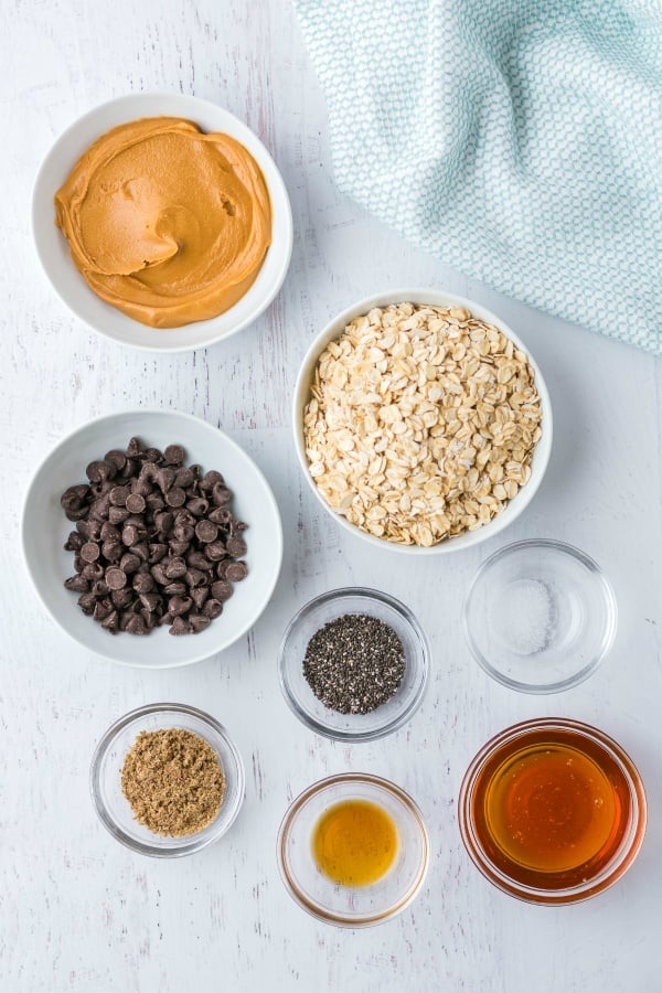 Ingredients in bowls - chocolate chips, oats, chia seeds, sugar, honey, vanilla, peanut butter and salt