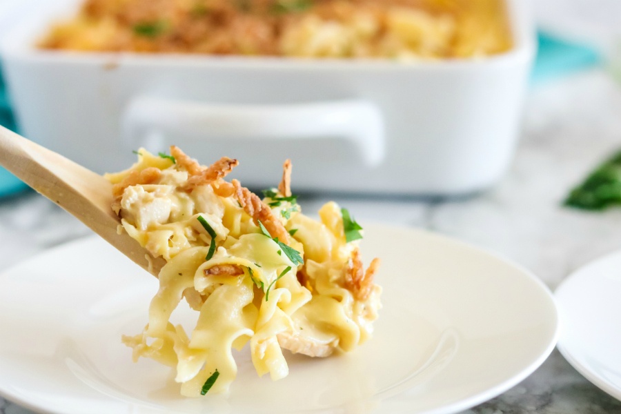 A scoop of french onion chicken noodle casserole being put on a white plate