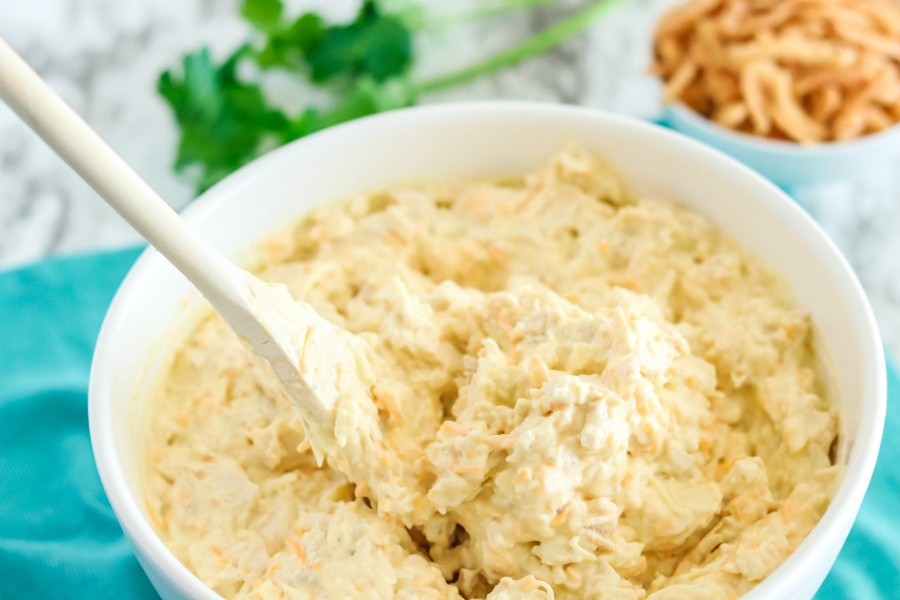 Chicken, cream of soup, onion dip, and shredded cheeses in a white bowl with a wooden spoon