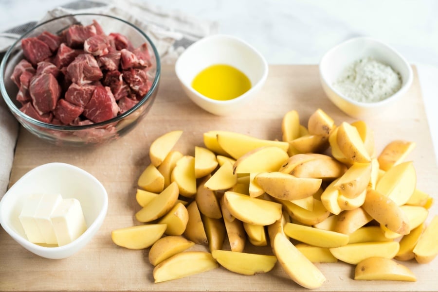 Potatoes slices, steak bites, butter, oil and seasonings on a cutting board