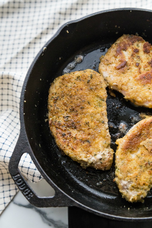 parmesan crusted pork chops cooking in a cast iron pan