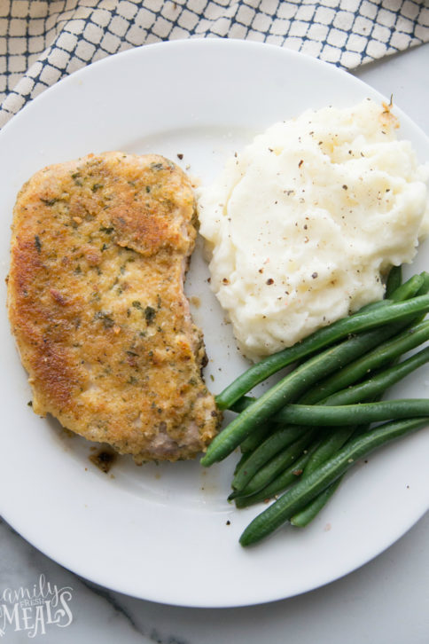 Top down picture of parmesan crusted pork chop on a white plate with green beans and mashed potatoes