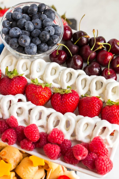 - raspberries, cherries, white chocolate pretzels, strawberries and blue berries, laid out on a platter, made to look like an American Flag