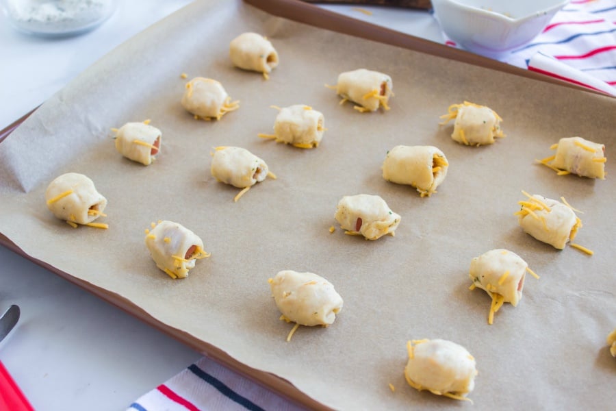 Hotdog pieces wrapped in cheesy dough on a parchment paper lined baking sheet