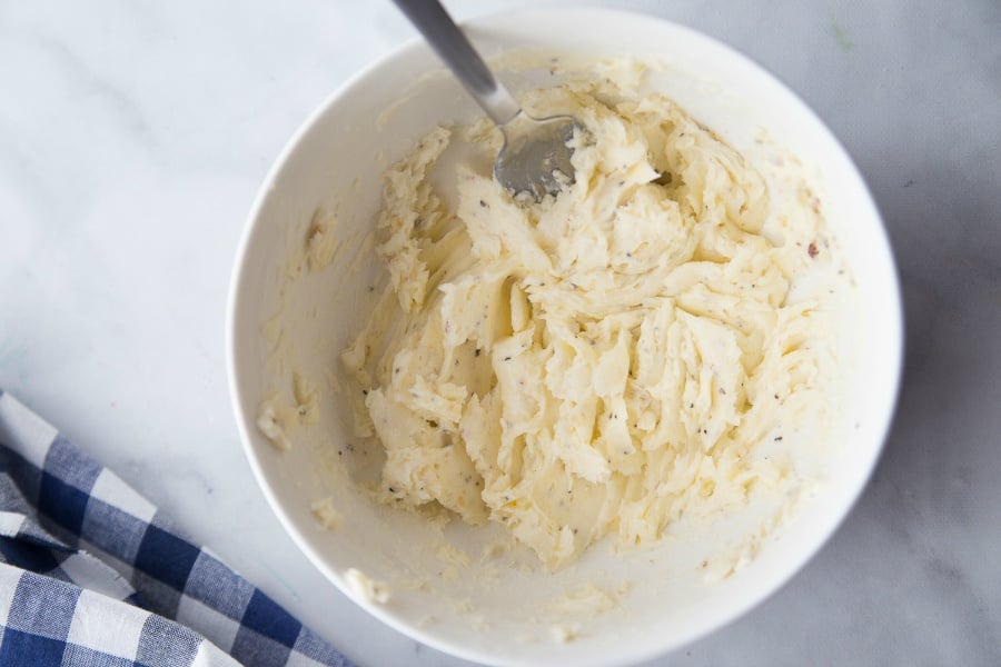 butter and seasoning being mixed in a white bowl with a fork