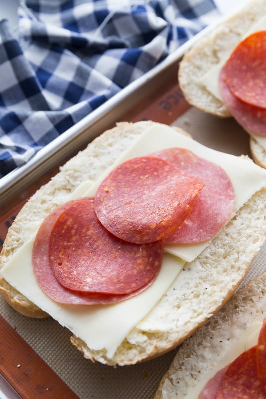 Hoagie roll topped with butter spread, cheese, salami and pepperoni